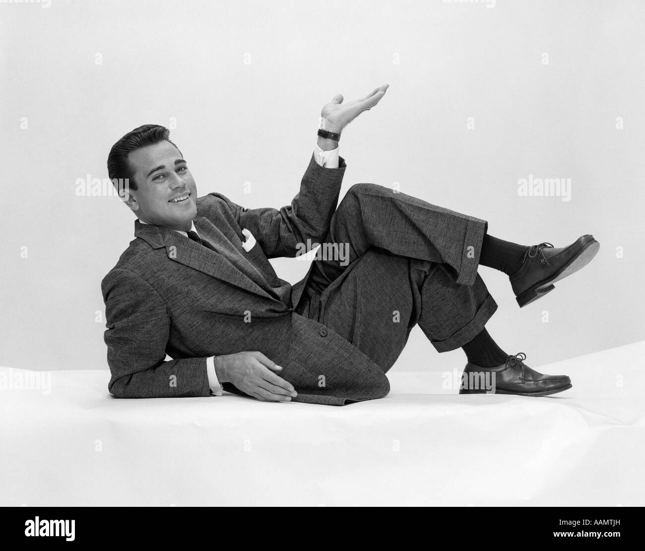 1950 El hombre en traje y corbata en el suelo apoyándose sobre el codo con las piernas cruzadas y la mano en el aire mirando a la cámara Foto de stock