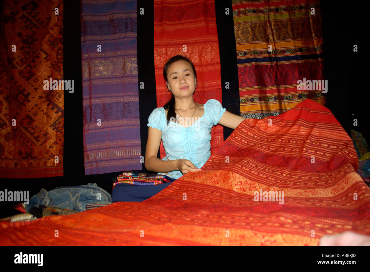 Mujer joven vende telas tejidas a mano de seda en el mercado nocturno de Luang Prabang Laos Foto de stock