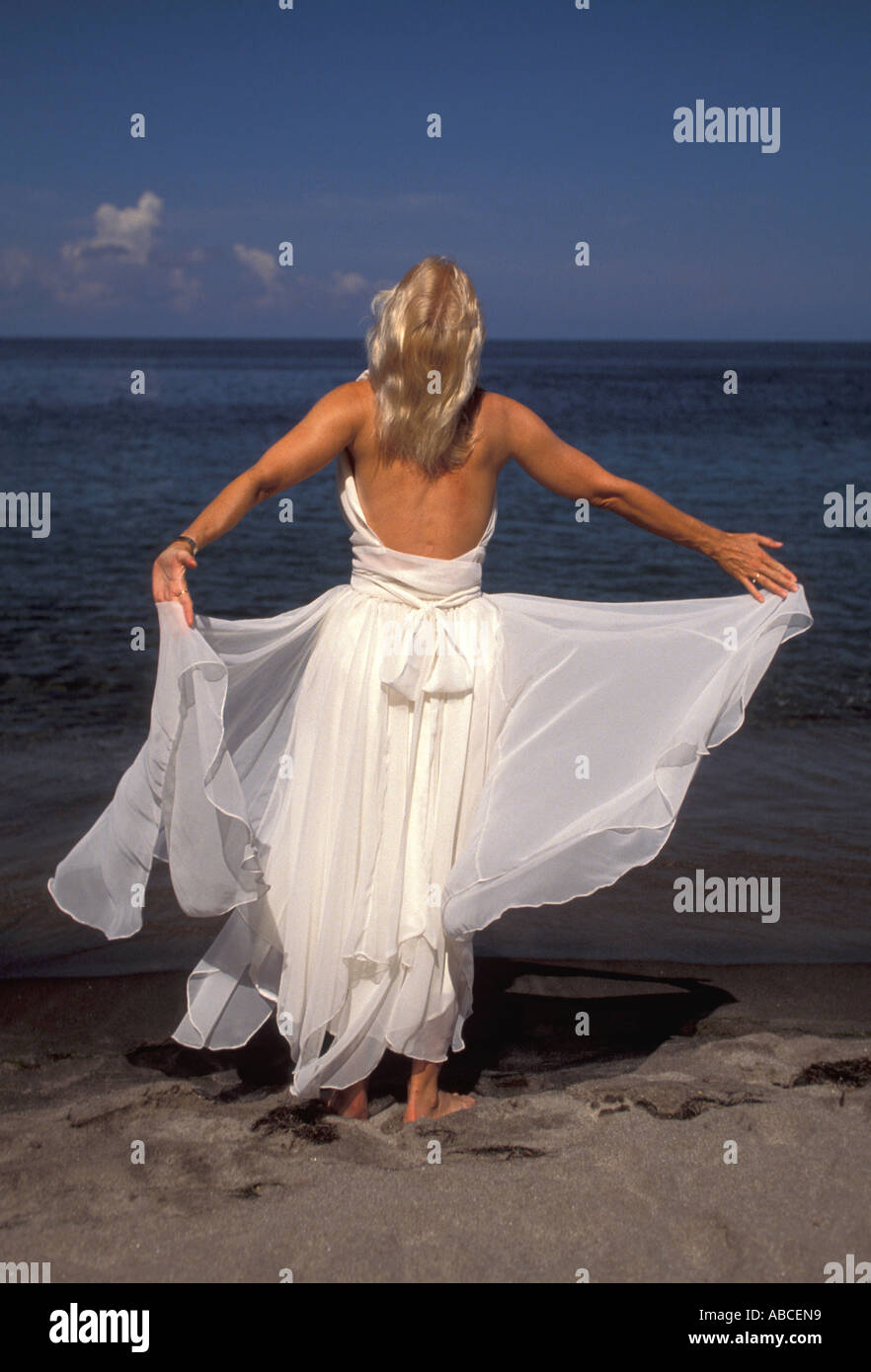 Boda caribeña playa mujer sola con blanco fluyendo bata formal está  descalzo sobre la arena de la playa enfrente del agua Fotografía de stock -  Alamy