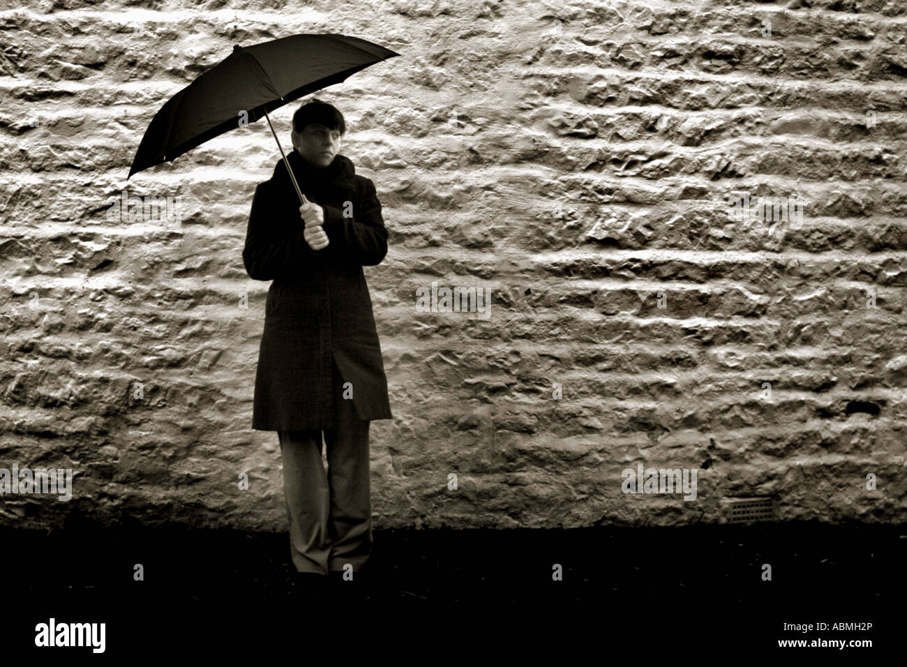 Foto horizontal de una un pelaje oscuro sosteniendo un paraguas negro en un día tempestuoso contra un ladrillo encaladas wa Fotografía de stock - Alamy