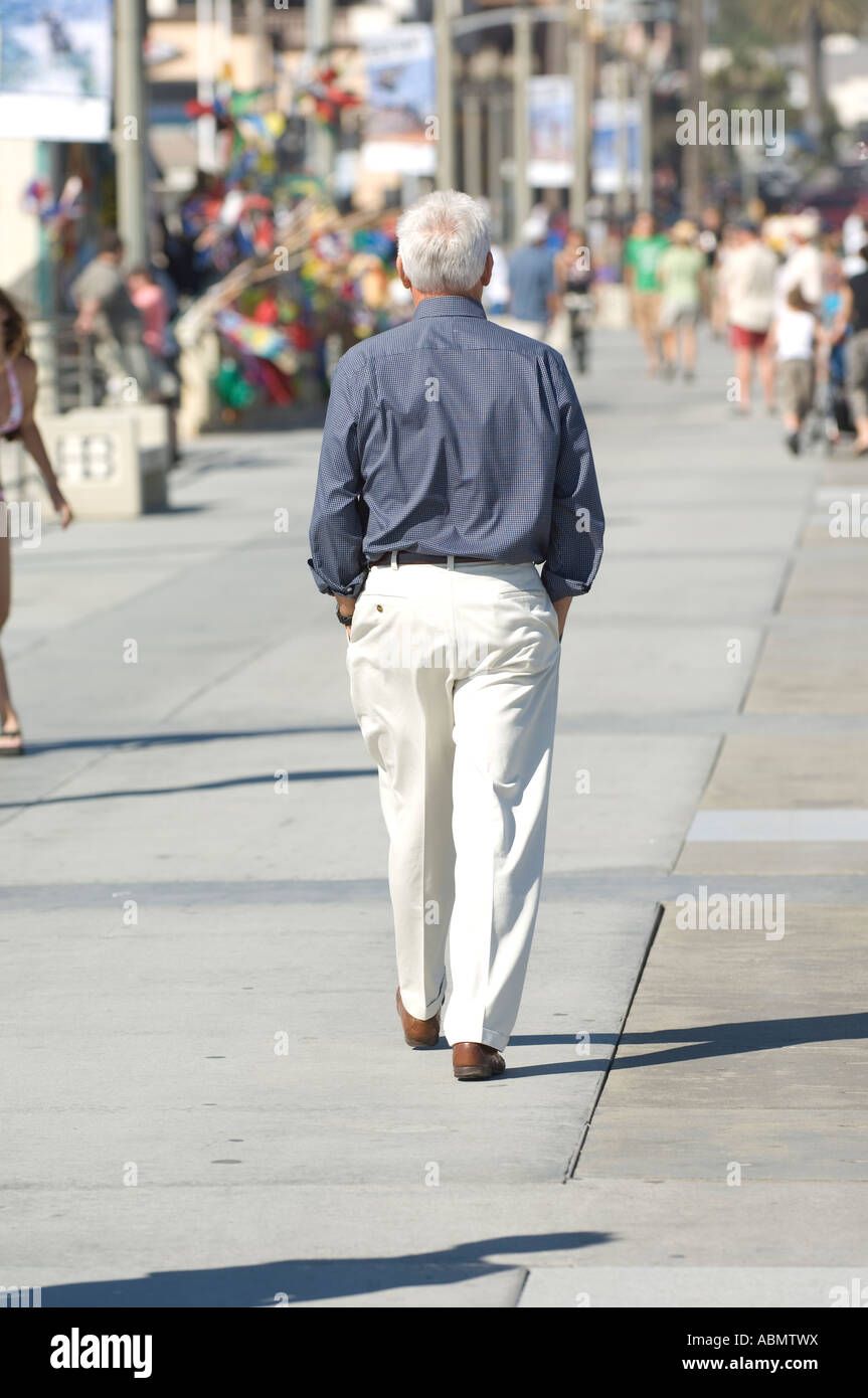 Caballero de cabellos blancos en gris, camisa blanca y pantalón lleva un  cuidado paseo por el Muelle de Huntington Beach Fotografía de stock - Alamy