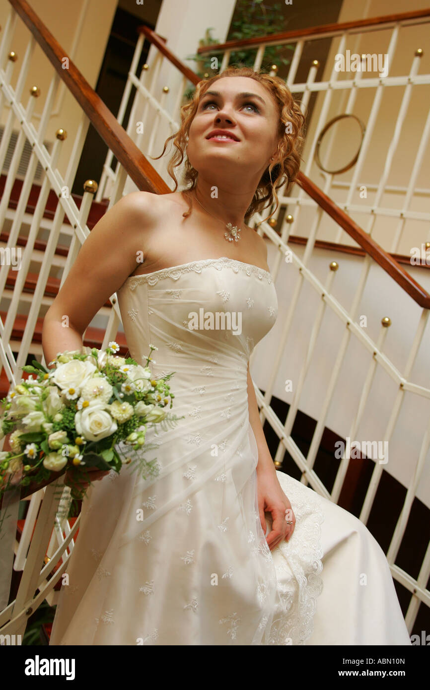 Un retrato de una novia en un vestido blanco retratada aquí bajando unas escaleras sosteniendo un ramo de flores. Foto de stock