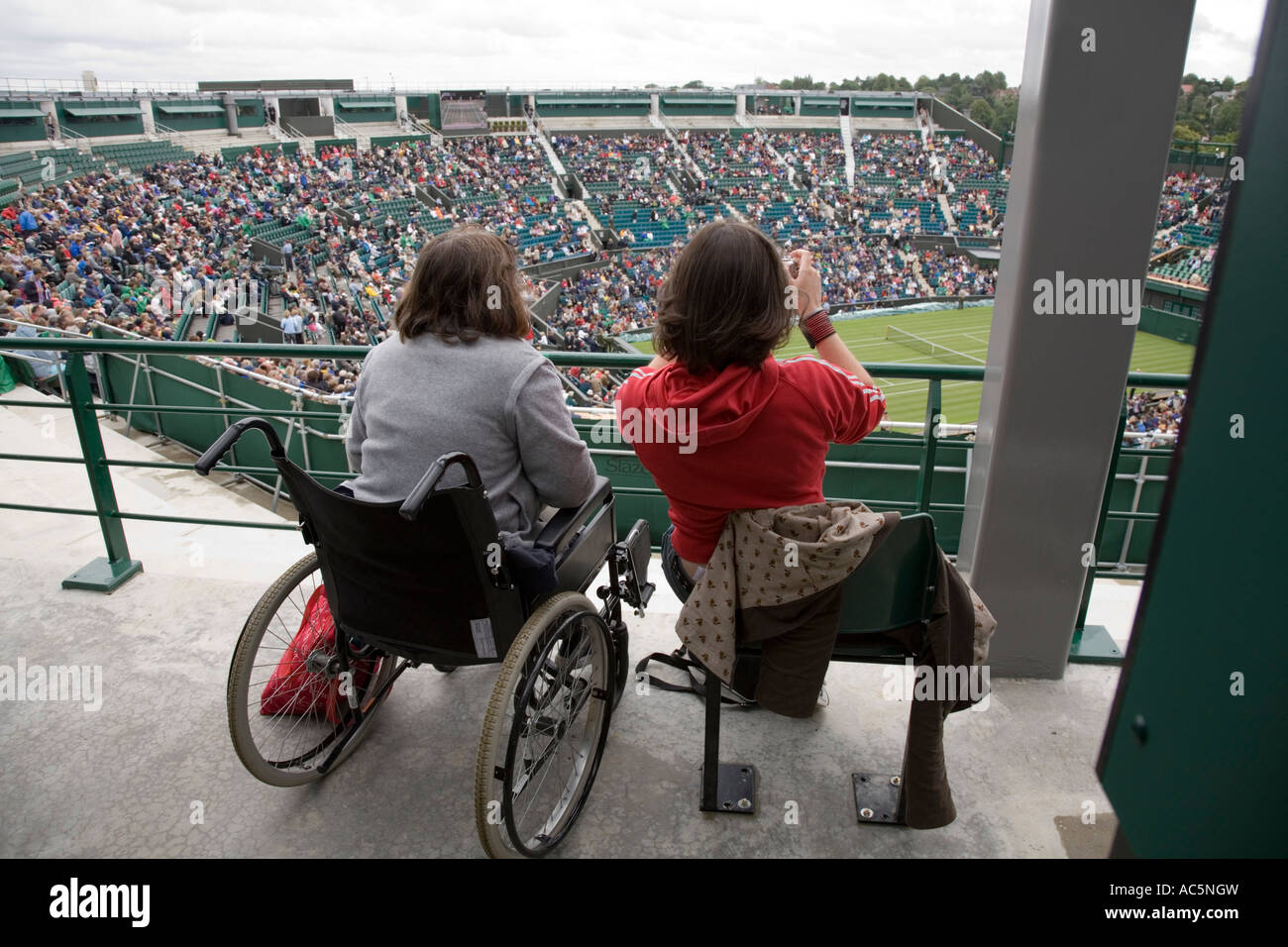 Mujer usuario de silla de ruedas y acompañante (tomando una fotografía) en el Campeonato de tenis de Wimbledon. En el Reino Unido. Foto de stock