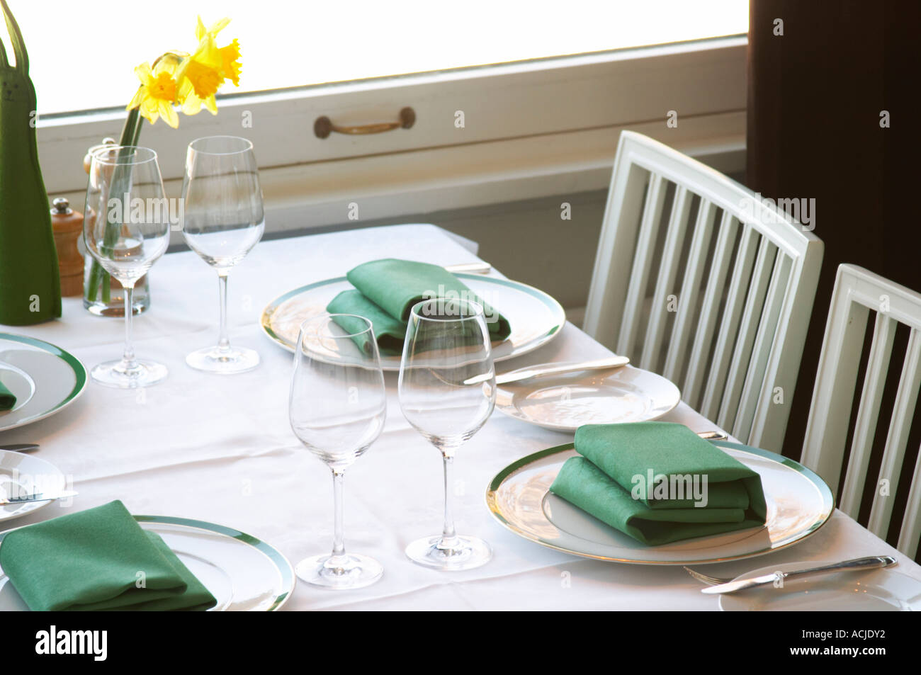 Una mesa de restaurante con manteles de lino blanco para cuatro personas,  con platos, cubiertos de plata y servilletas de color verde y amarillo  Narciso Pascual lily flor sobre la mesa. Ulriksdal