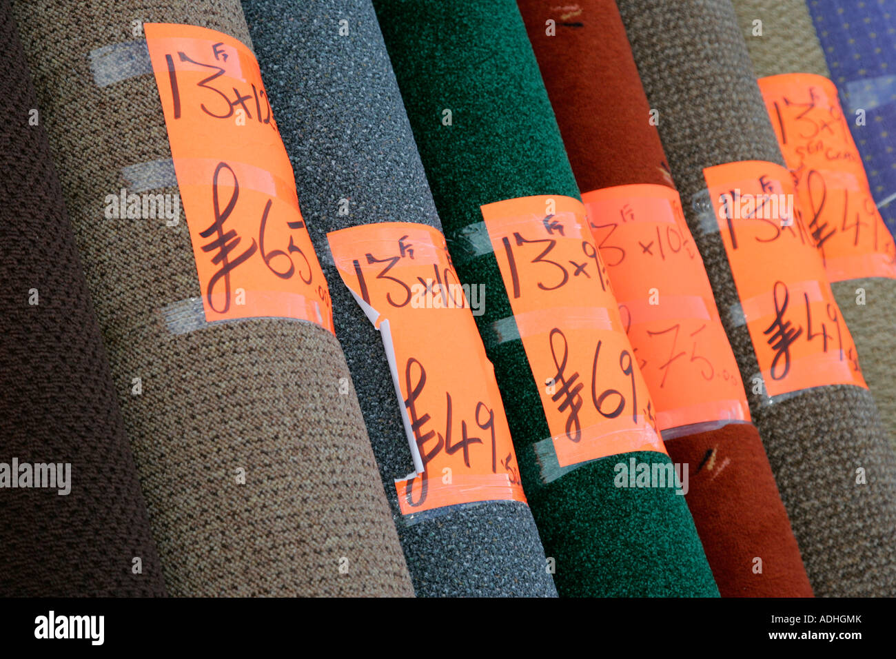 Rollos de alfombra hogar amontonadas en la pantalla fuera de una tienda de alfombras con etiquetas de precios en libras y mediciones imperial Foto de stock