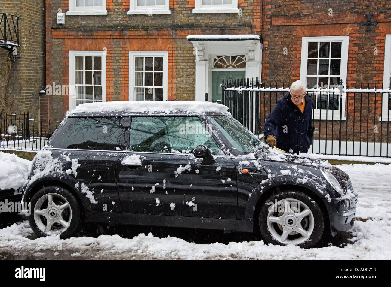 Hombre raspaduras nieve de Mini Cooper coche aparcado en la calle de Londres Iglesia Fila Hampstead Inglaterra Foto de stock