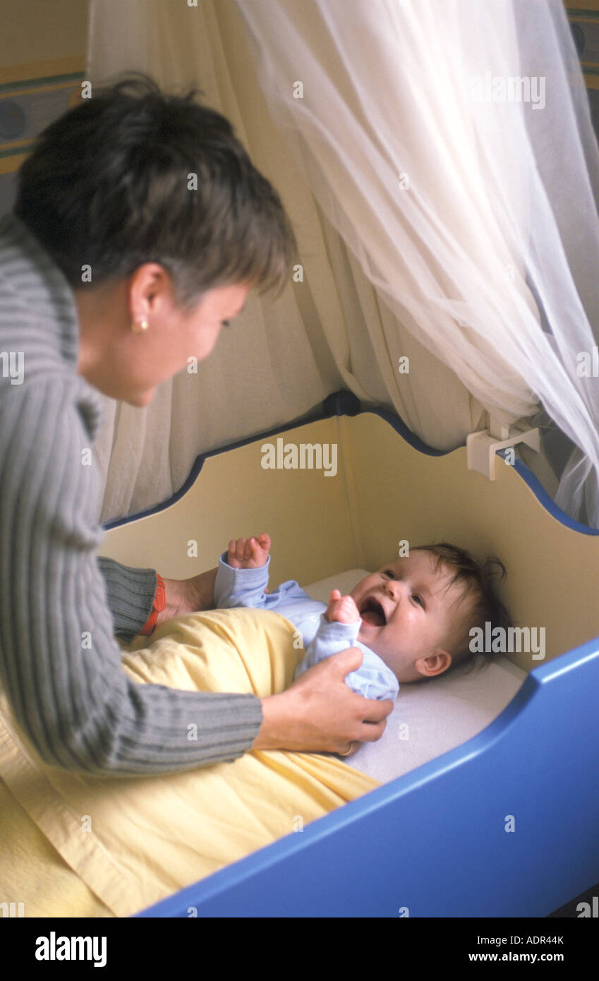 La madre está poniendo a su bebé en la cama Foto de stock