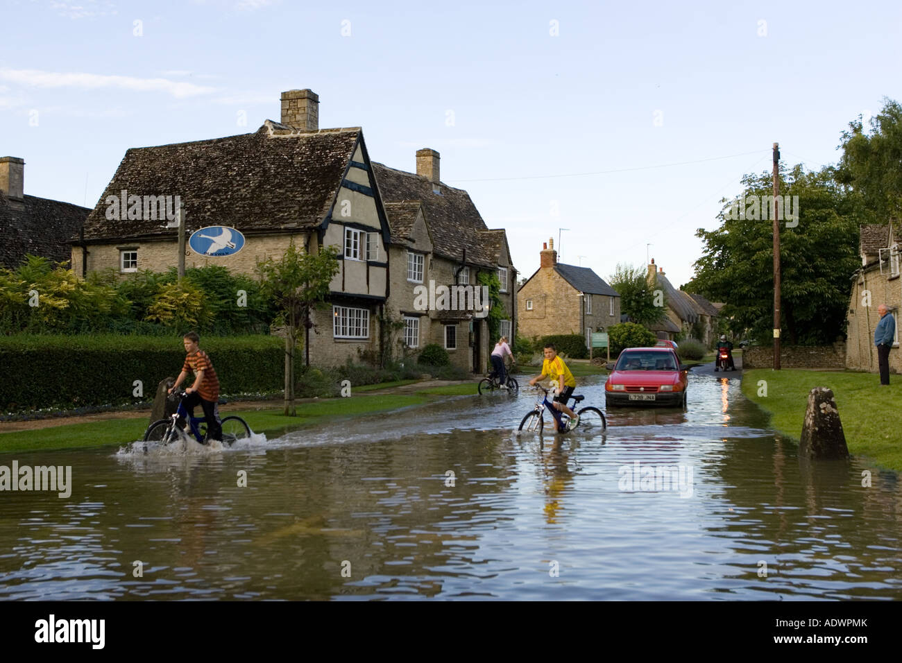 Los niños en sus bicicletas a través de las aguas de la inundación en Minster Lovell los Cotswolds, Oxfordshire, Inglaterra, Reino Unido Foto de stock