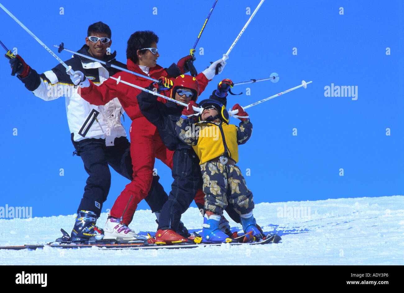 Esquí en familia, la familia de pie uno después del otro, sosteniendo bastones de esquí en posición vertical Foto de stock