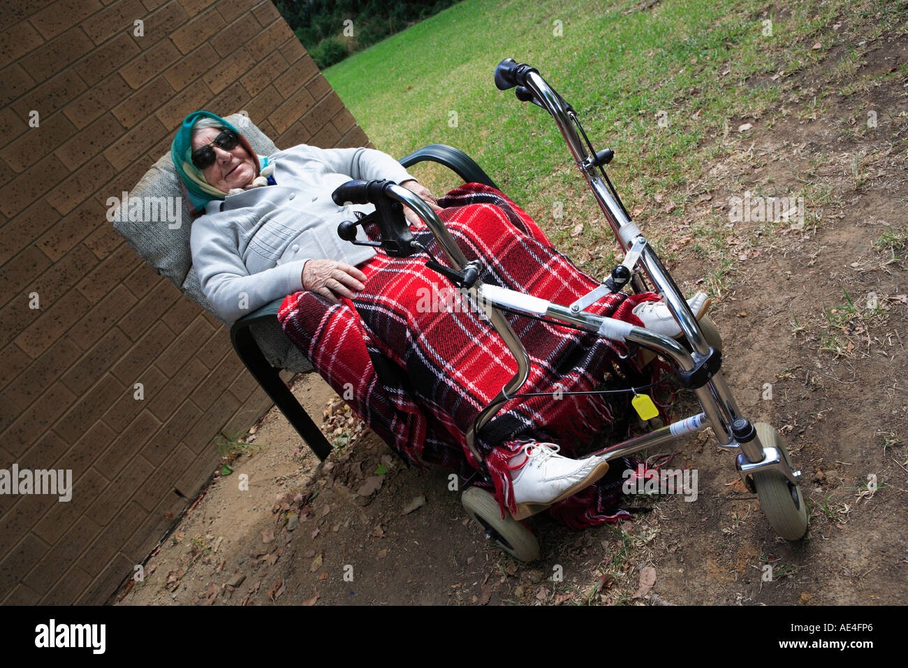 Anciana noventa, sentado afuera con los pies descansando en sus tres ruedas, Walker Foto de stock