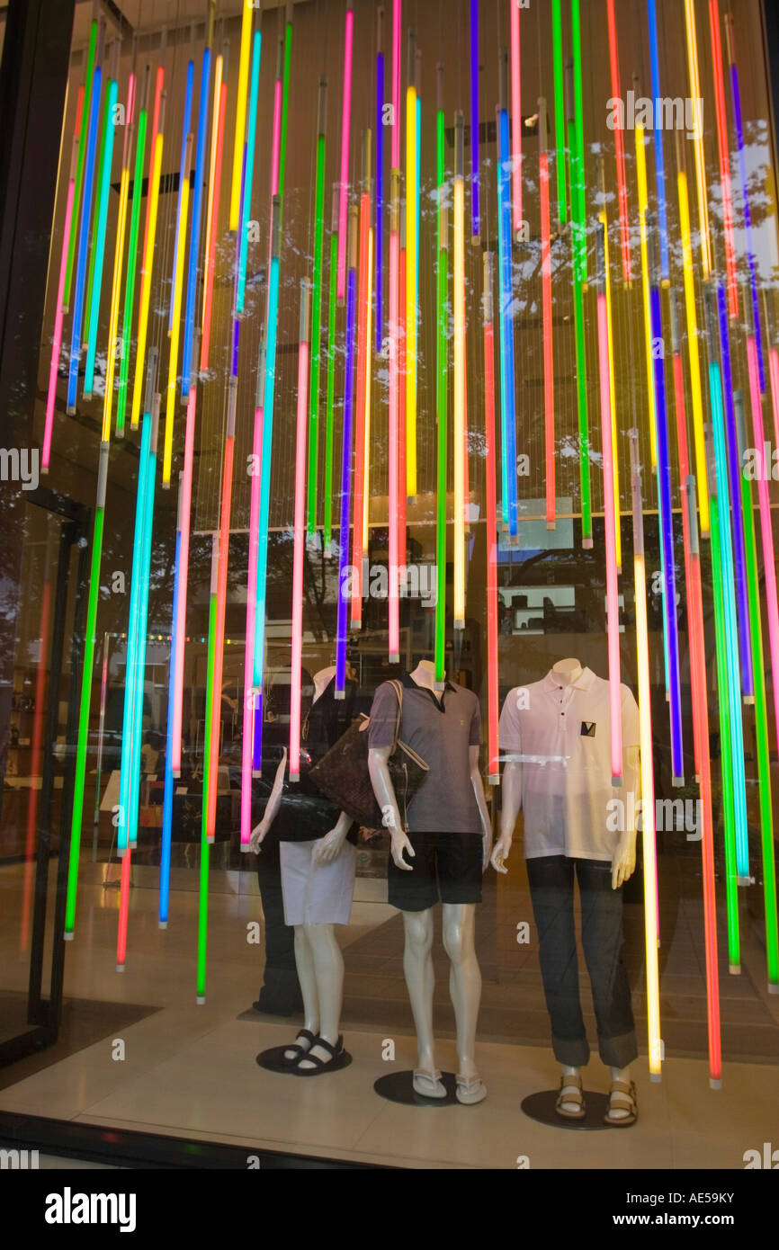 Colorido escaparate en una tienda de ropa con tres maniquíes y muchos tubos verticales de coloridas luces fluorescentes Foto de stock