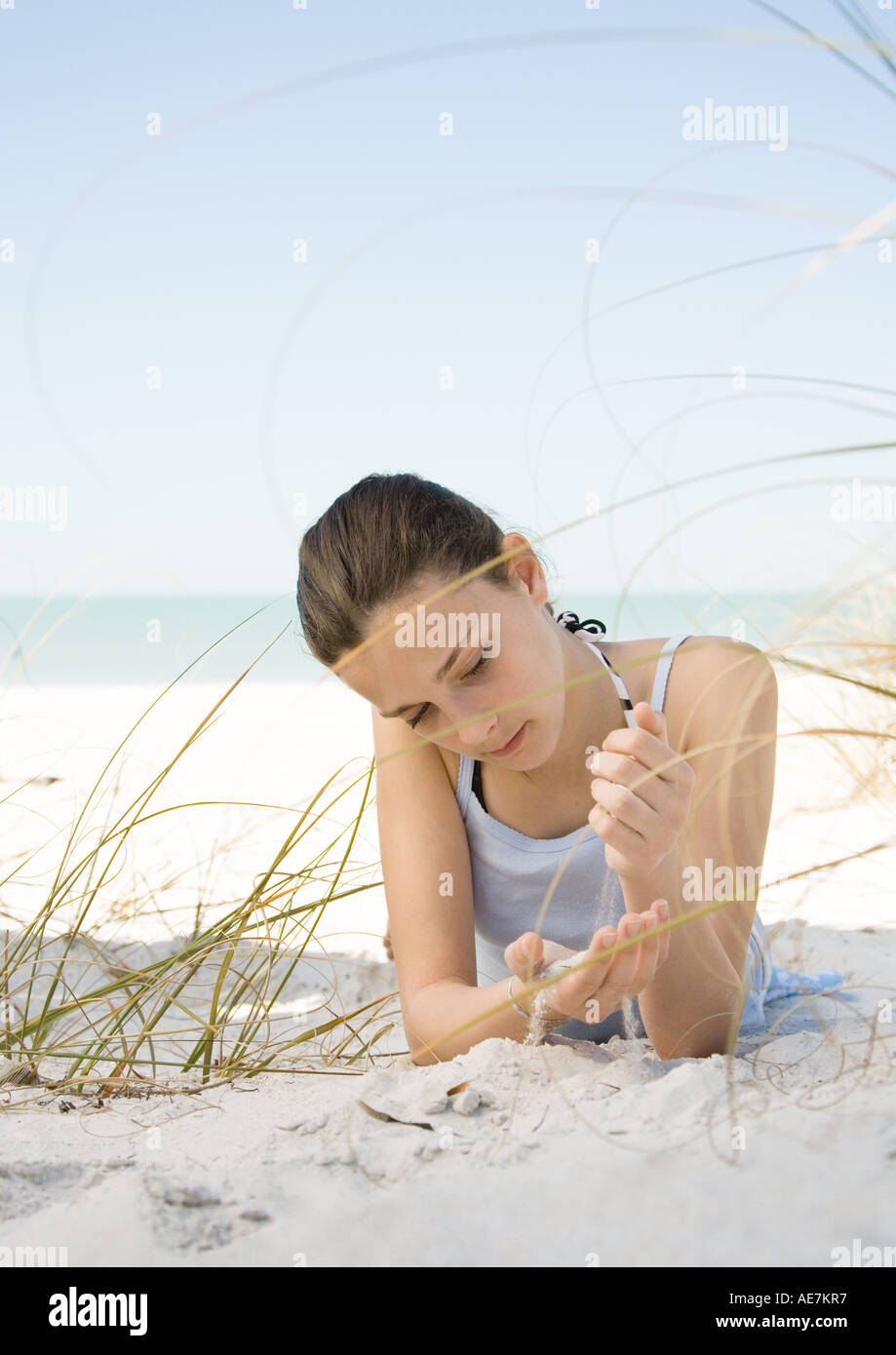 Chica tumbado en la playa de arena, dejando correr a través de manos Foto de stock