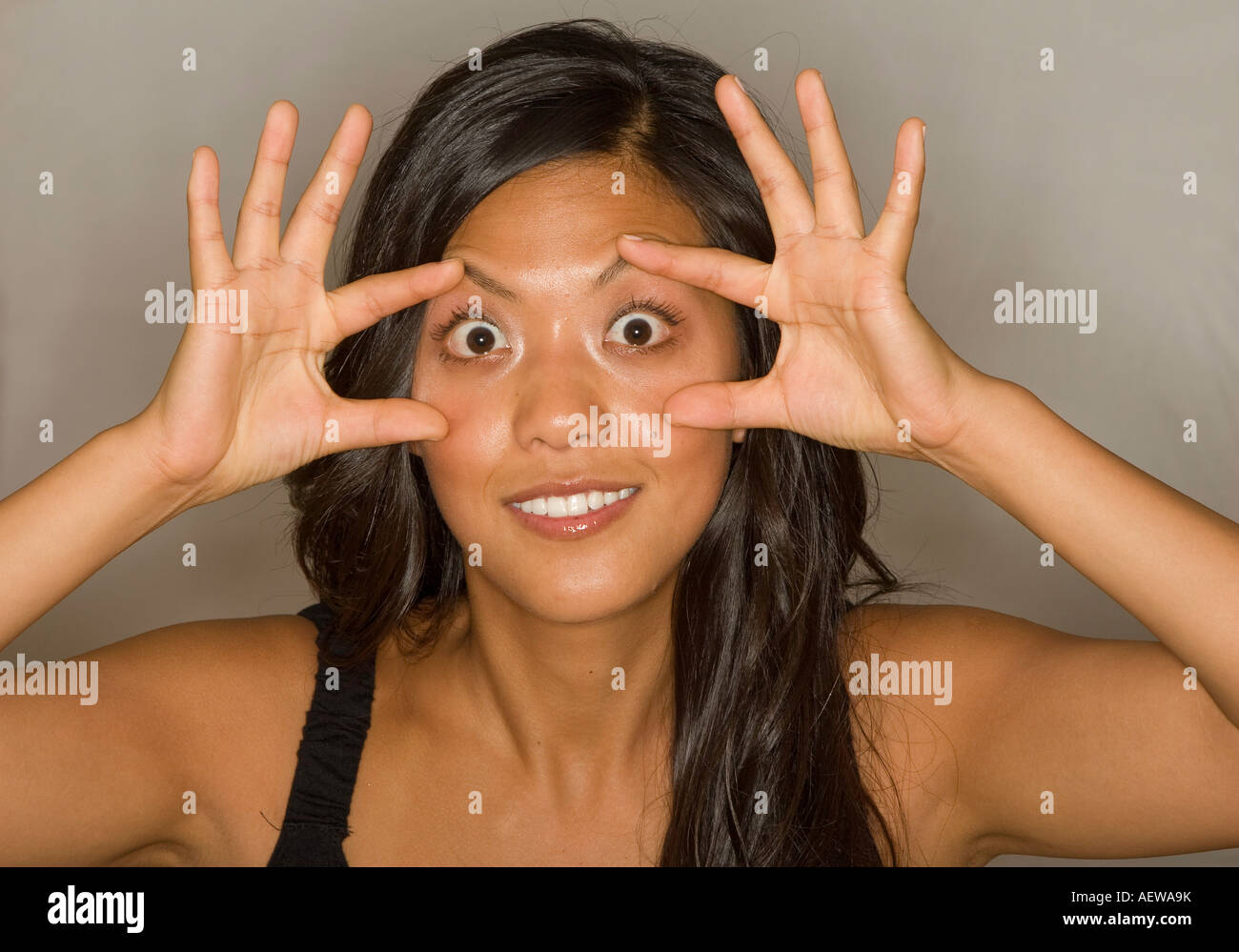 Hermosa joven mujer asiática abultamiento de los ojos con los dedos extendidos Foto de stock
