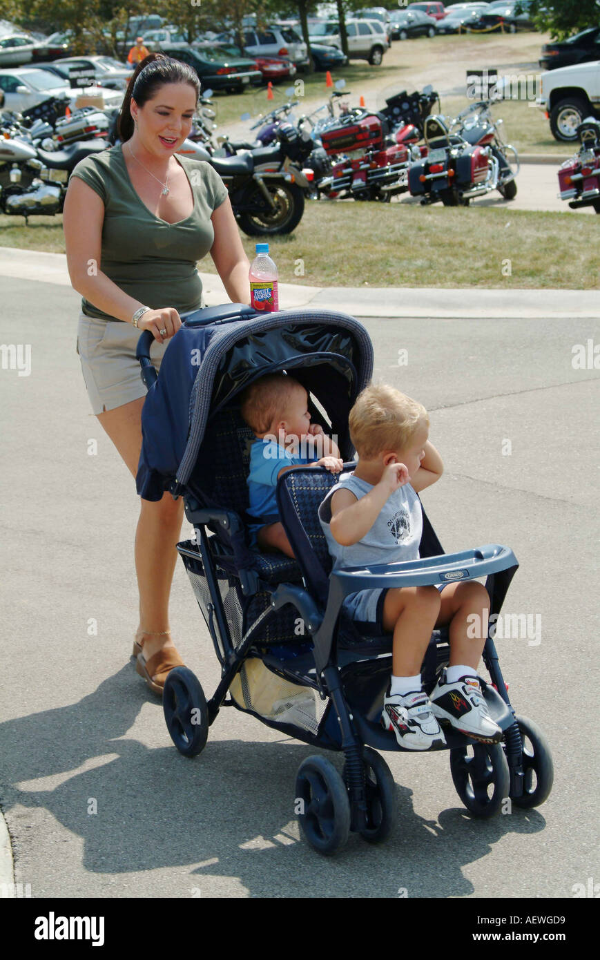 Una en pantalones cortos y camiseta dando un con sus dos hijos en el cochecito Fotografía de -