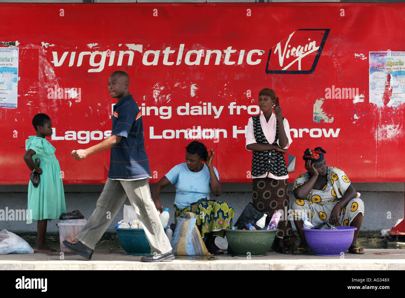 Un hombre camina pasado las mujeres vendiendo productos en frente de una virgen Airlines poster Lagos, Nigeria Foto de stock