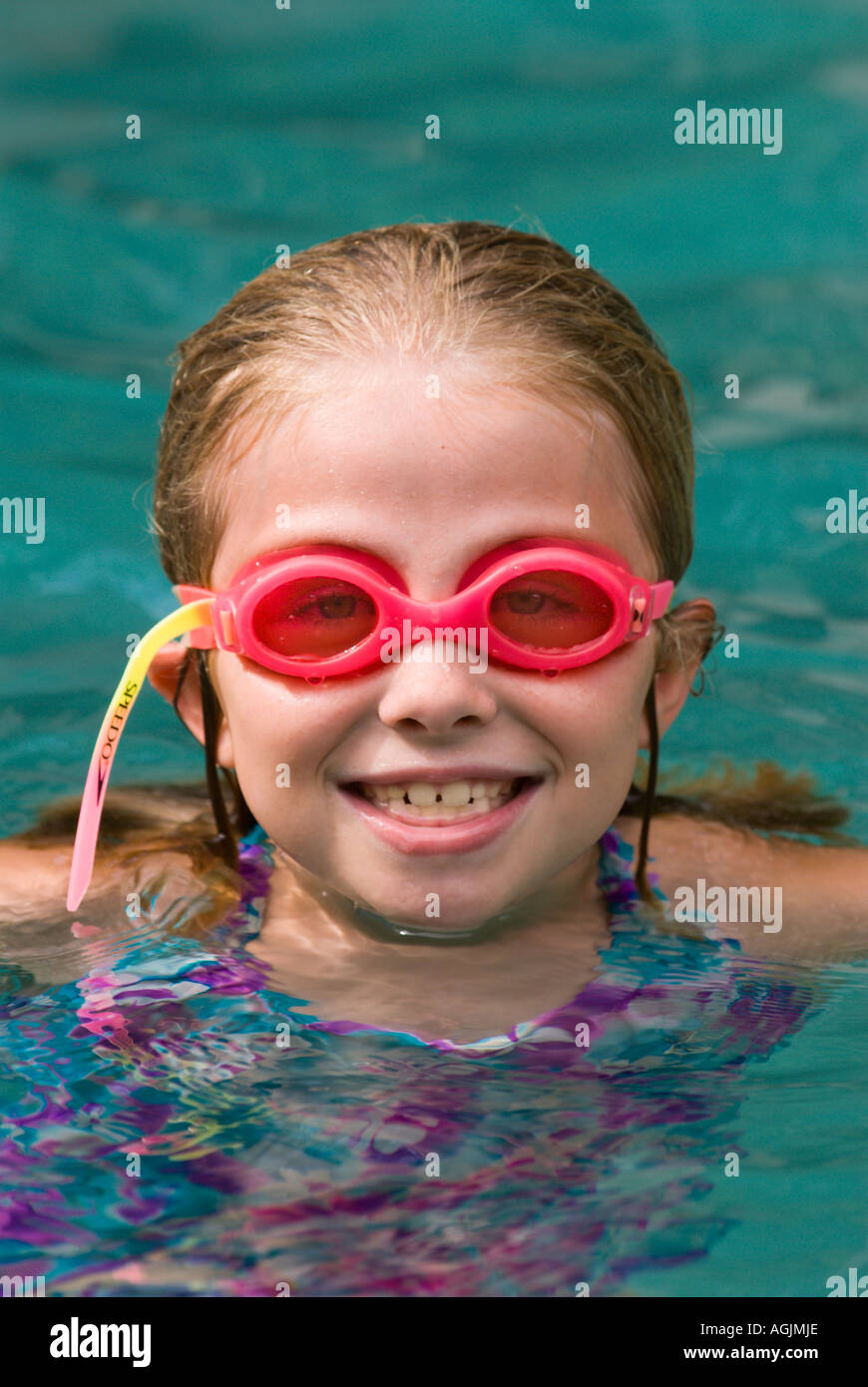 Una niña divirtiéndose en la piscina familiar llevaba gafas de natación rosa y sonriente en el modelo de la y liberados Fotografía de stock -
