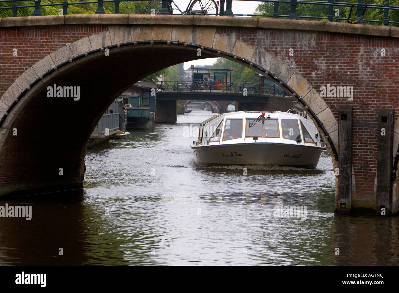 Canal Boat viajando bajo un puente sobre un canal, cerca del río Amstel en Amsterdam, Países Bajos Foto de stock