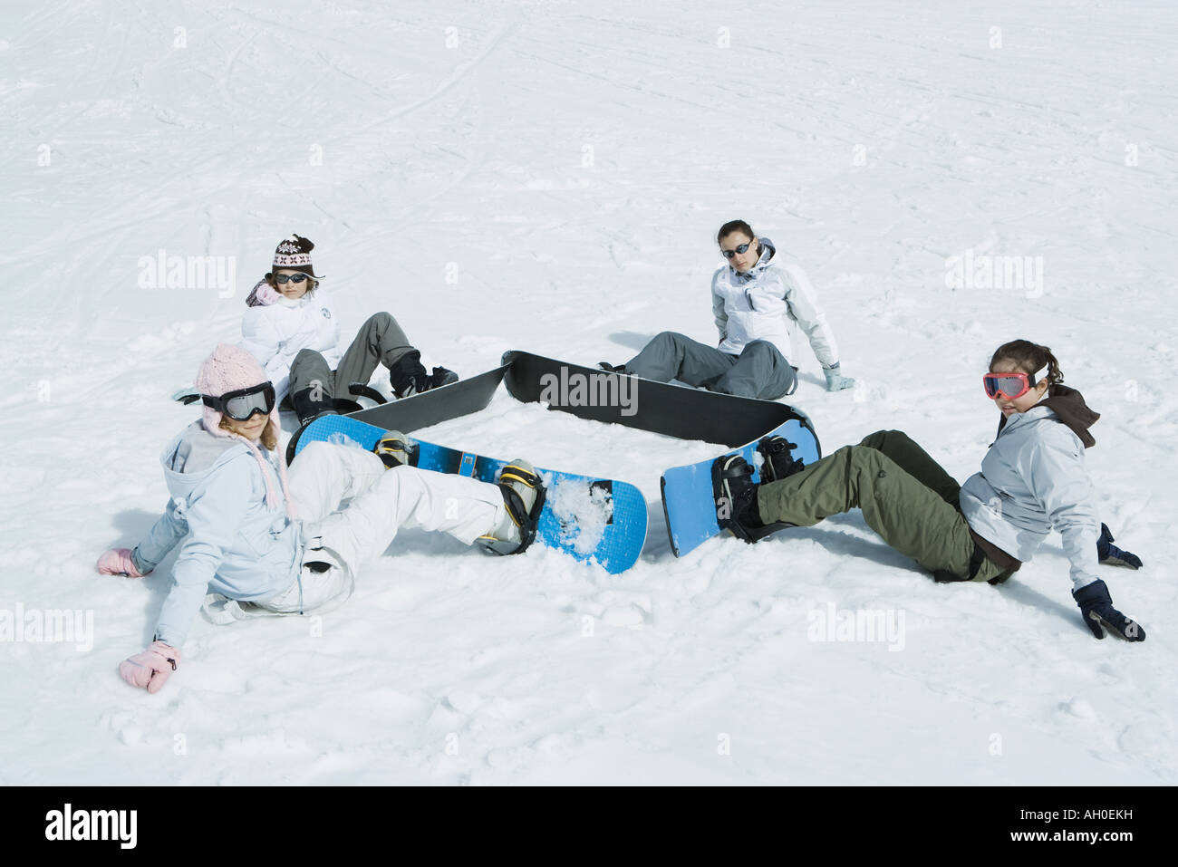 Cuatro jóvenes snowboarders, sentados en el suelo en una plaza, mirando a la cámara Foto de stock