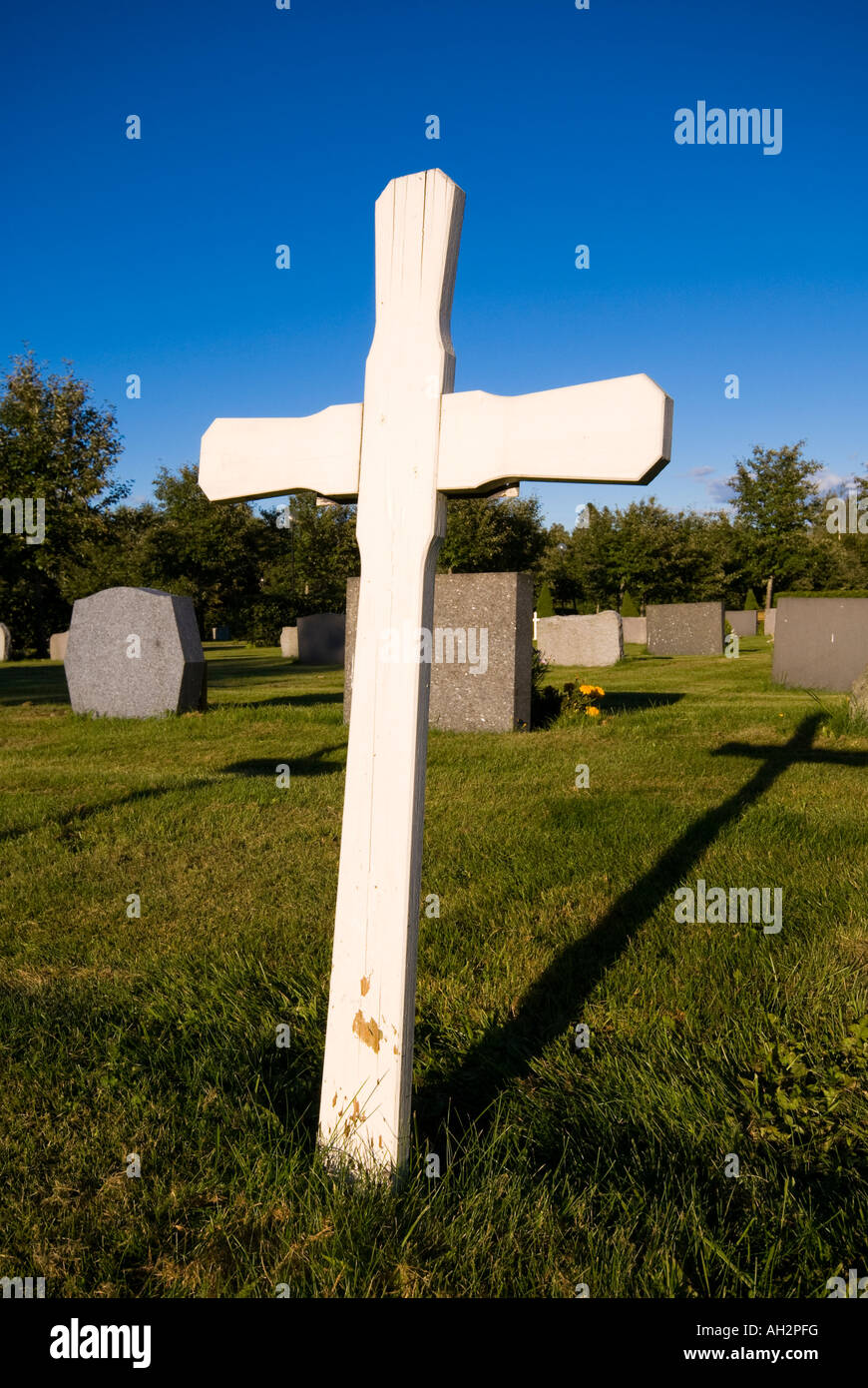 Cruz de madera blanca en el cementerio dando larga sombra negra Foto de stock