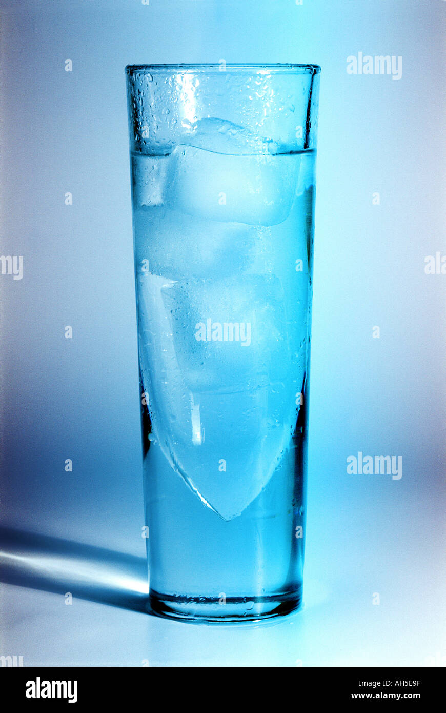 Vidrio en una luz azul con sombra conteniendo agua y cubo de hielo Foto de stock