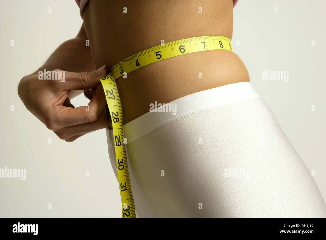 Señorita midiendo su cintura con una cinta métrica amarilla horizontal Foto de stock