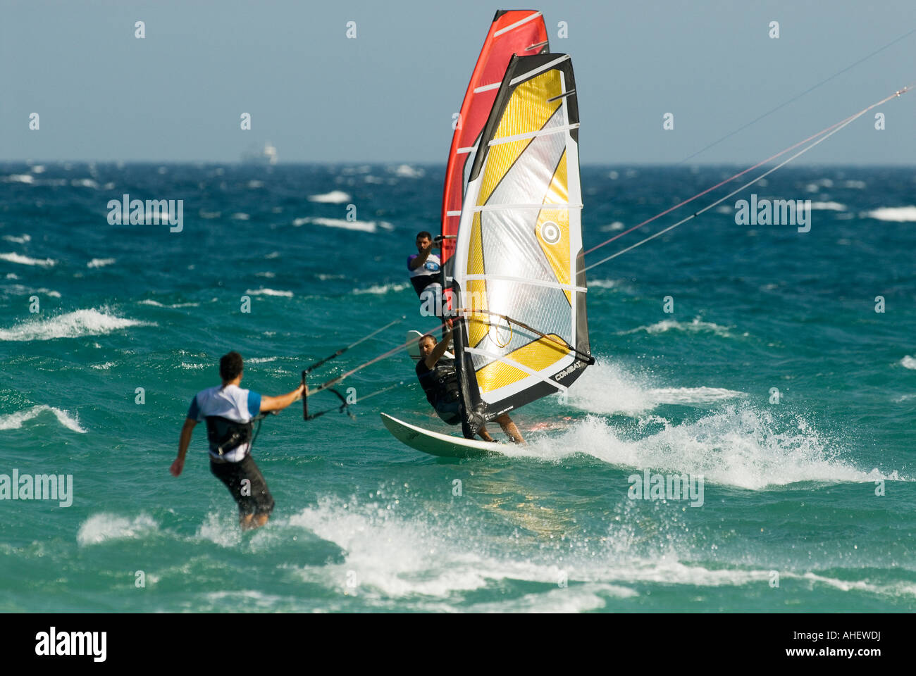 Dos tablas de windsurf y un kitesurfer montar las olas en el mar mediterráneo. Foto de stock