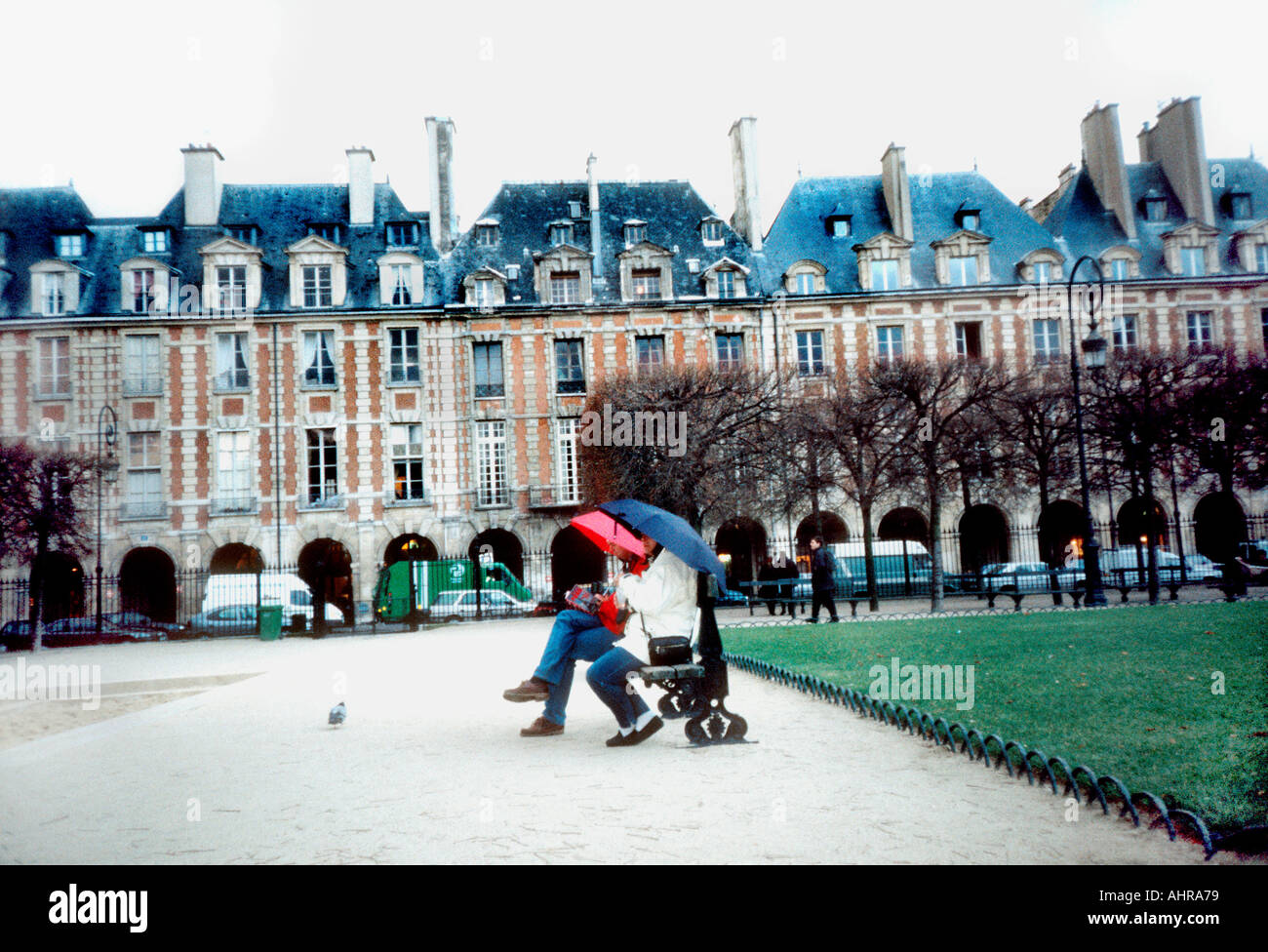 París Francia Parks Pareja sentado en el banco del parque con sombrillas en la arquitectura histórica 'Place des Vosges' de la lluvia, Le Marais Foto de stock