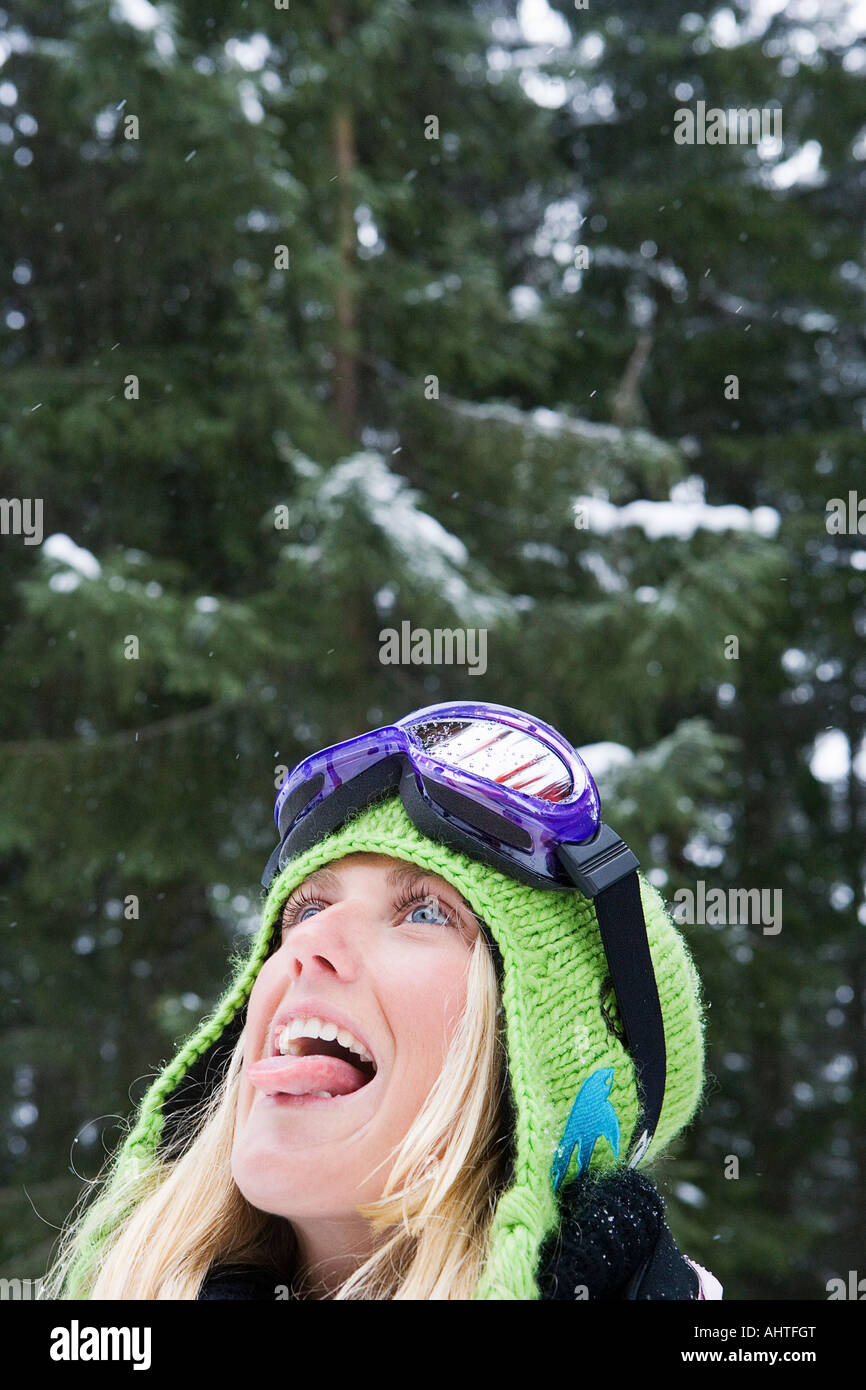 Close-up de joven mujer rubia vistiendo ropa de esquí lengua fuera para coger la nieve Foto de stock