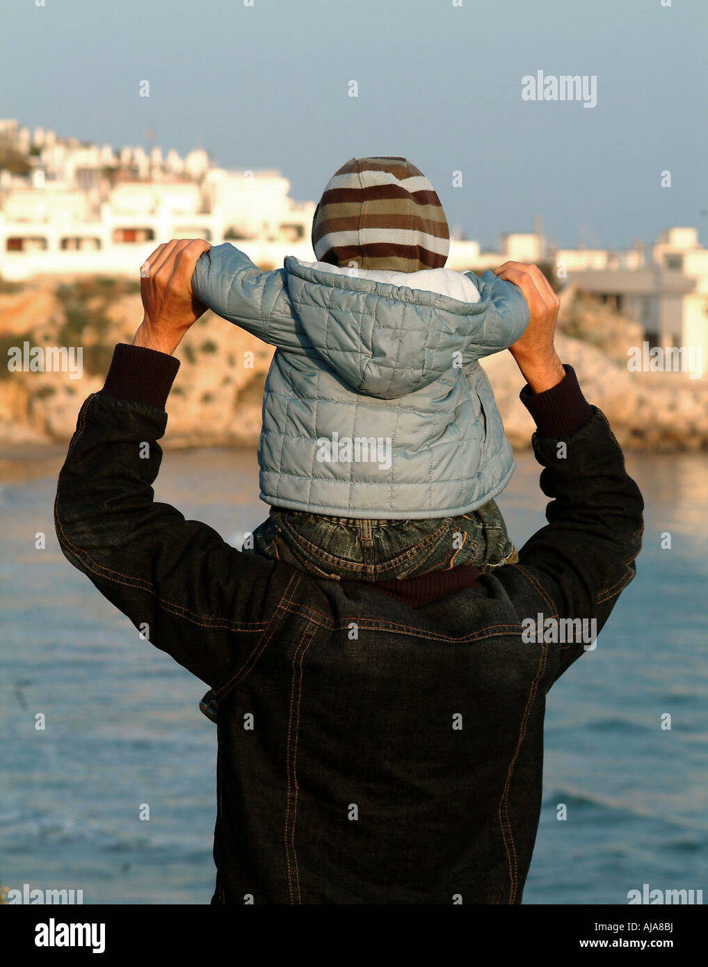 Un niño se sienta sobre los hombros de su padre al dar un paseo por el océano Foto de stock