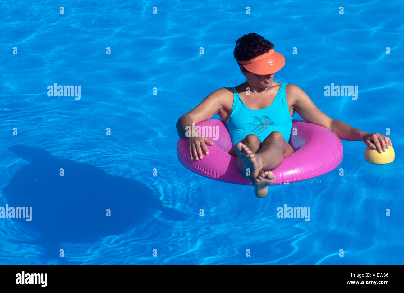 Mujer sentada sobre neumáticos flotantes en la piscina, vistiendo el traje de baño azul Foto de stock