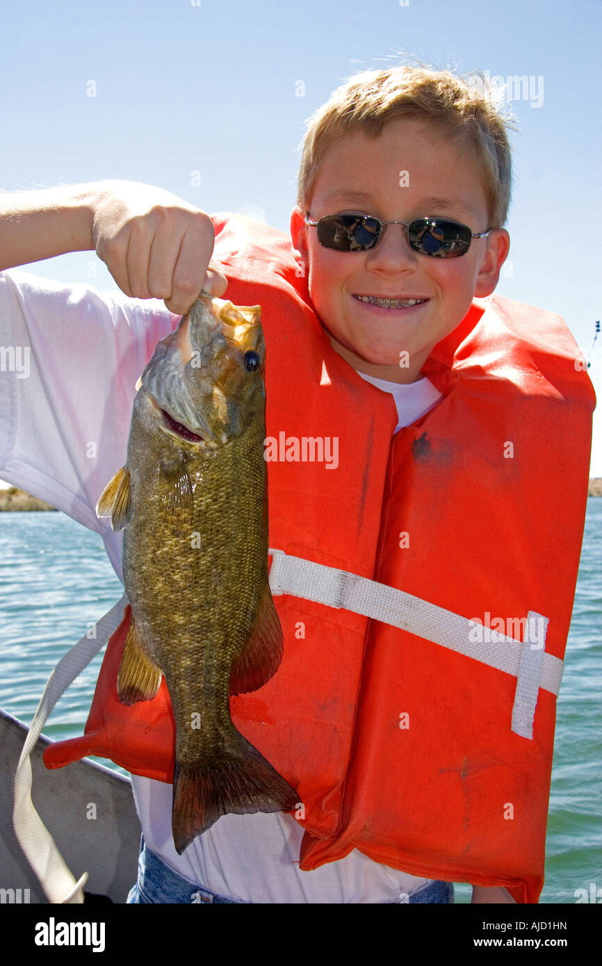 Un muchacho de doce años vistiendo un chaleco salvavidas y sosteniendo un bass atrapó mientras pescaba en Idaho MR Foto de stock