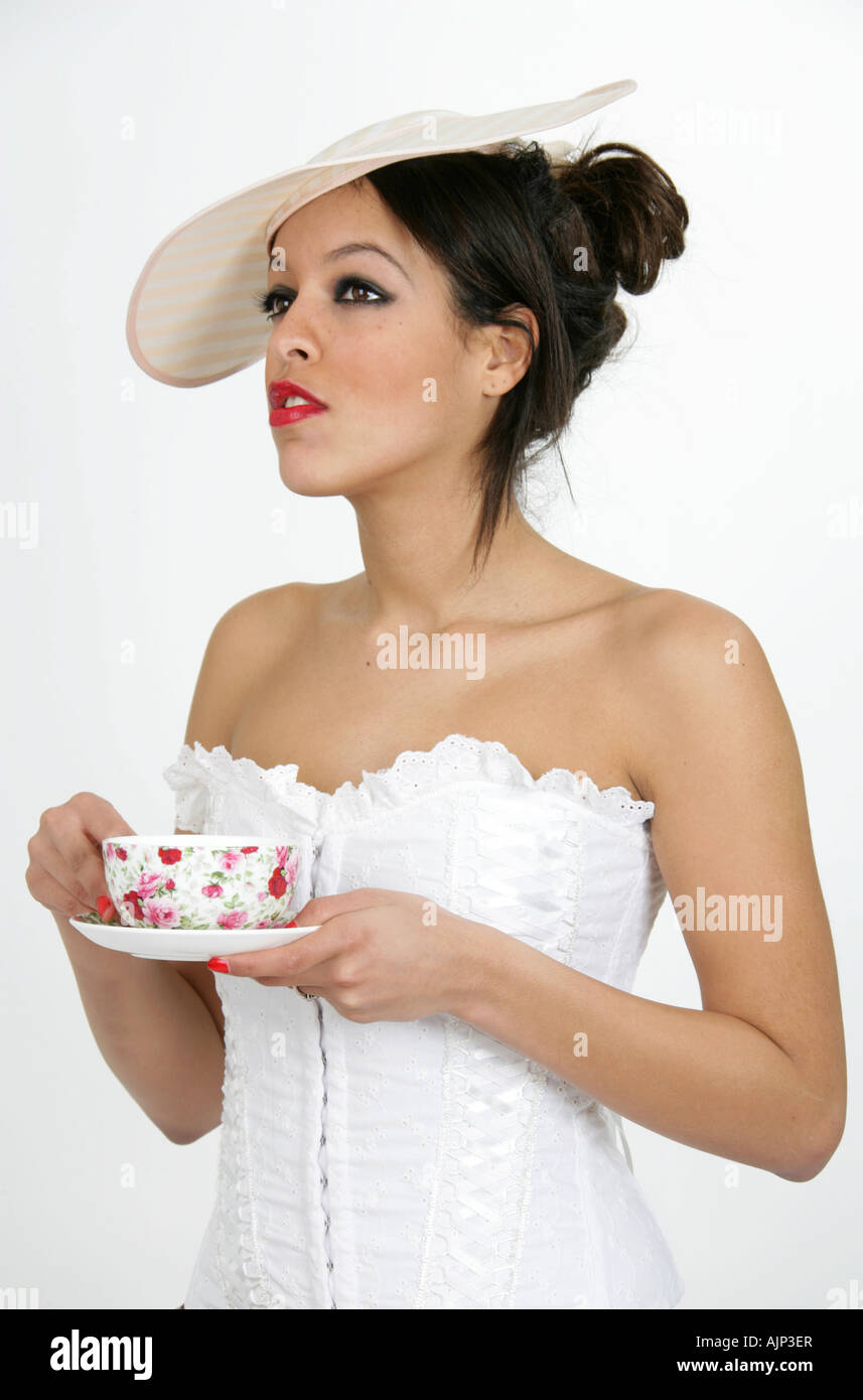 Vestida con un corsé blanco y sombrero de beber una taza de té Foto de stock