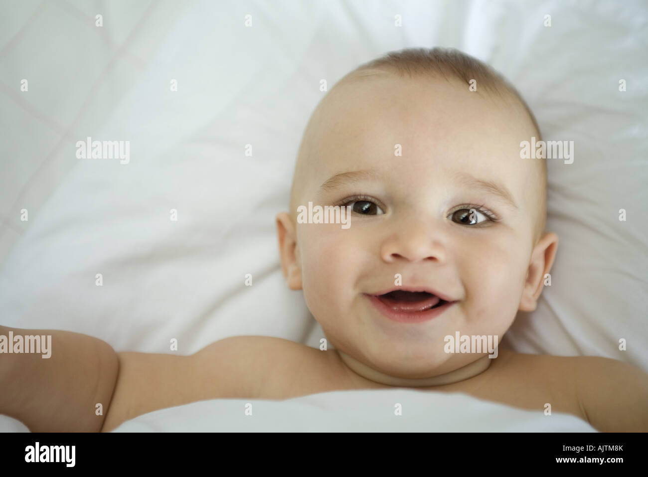 El bebé en la cama, debajo de cubiertas, sonriendo Fotografía de stock