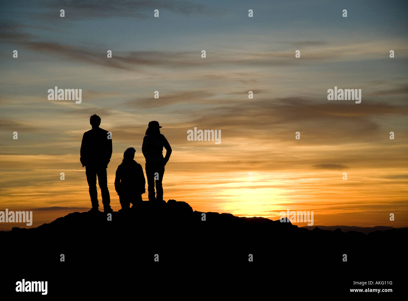 Tres personas viendo la puesta de sol desde la cumbre de Arthurs Seat en Holyrood Park Edimburgo Scotland Reino Unido Foto de stock