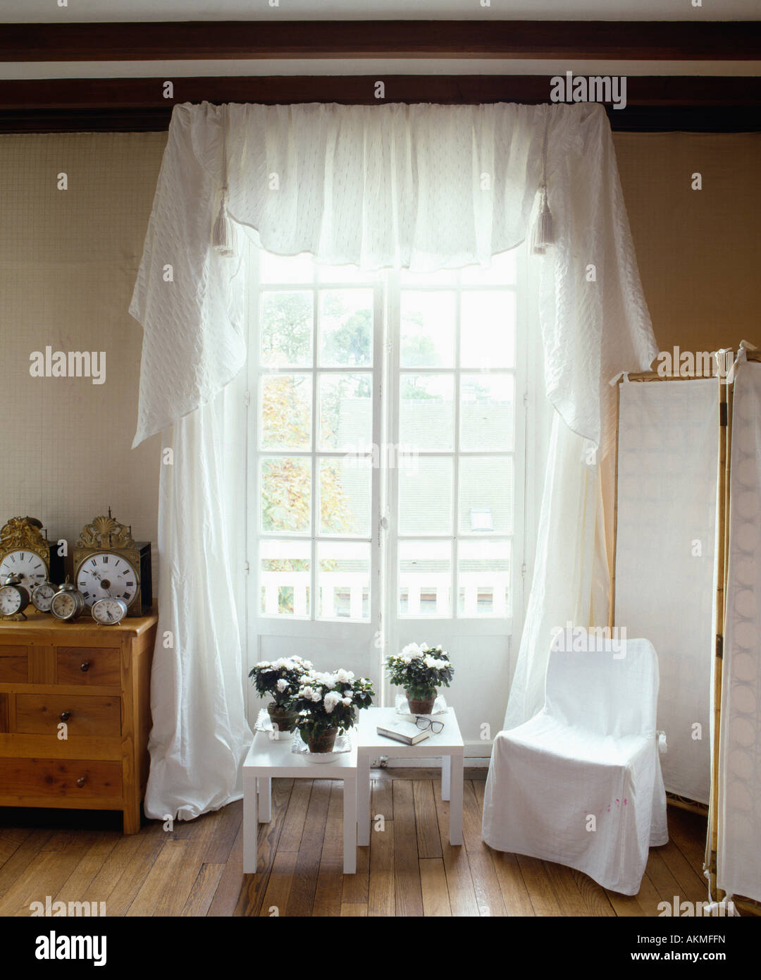 Pequeño cuadro blanco y blanco loosecover en silla enfrente de las puertas francesas con cortinas de velo blanco Foto de stock