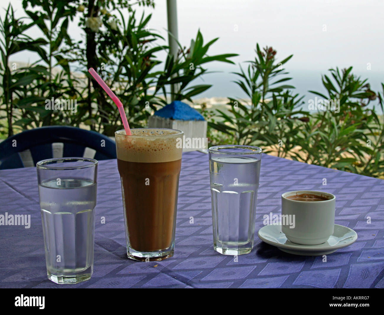 Café Frappé griego y café frío con espuma y dos vasos llenos de agua fría sobre una mesa horizontal con Mediterran Mar Foto de stock
