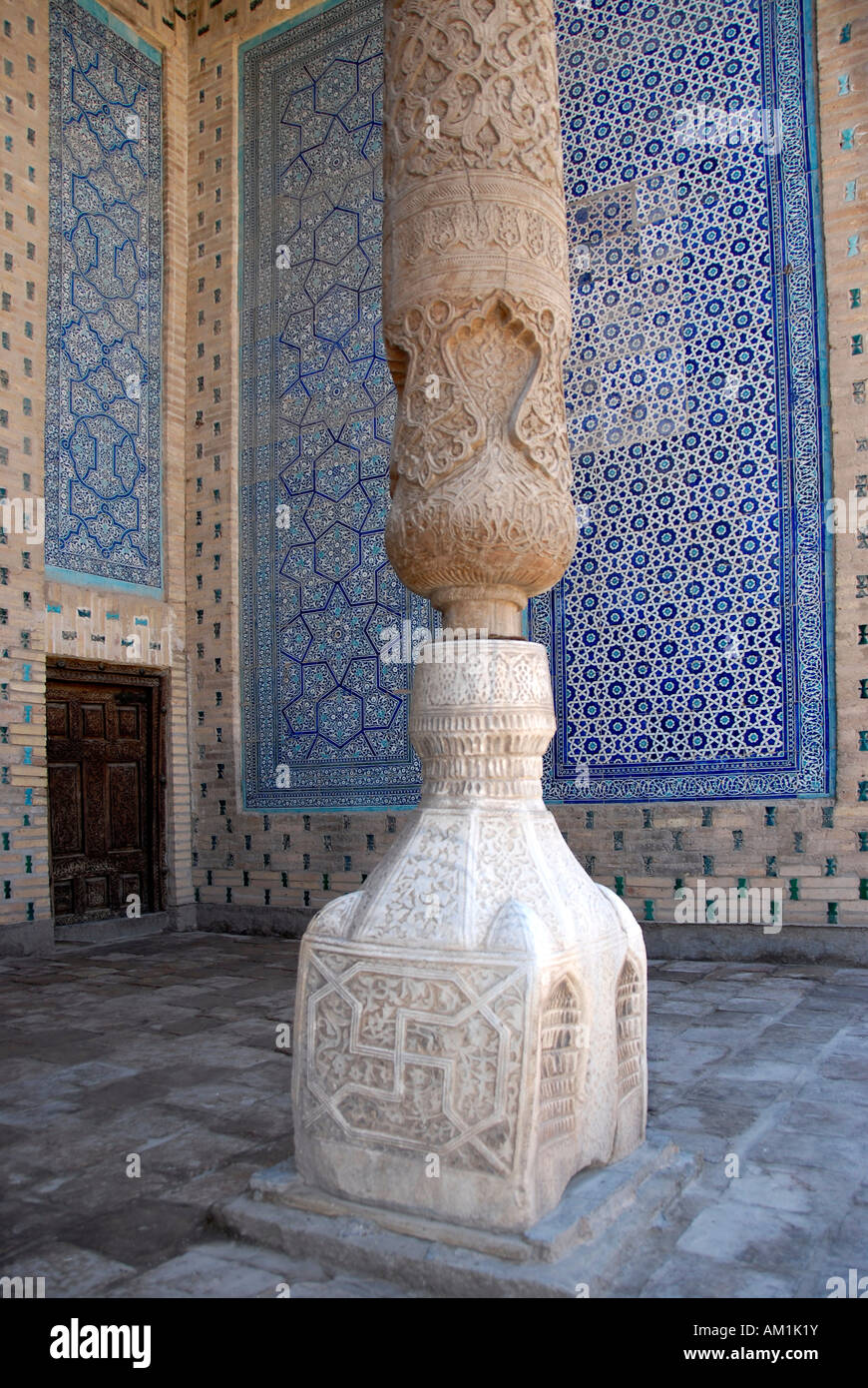 Columna de madera tallada, sobre un zócalo de mármol decorado con paredes decoradas con fino azul maiolica Tash Hauli Palace Khiva Uzbekistán Foto de stock