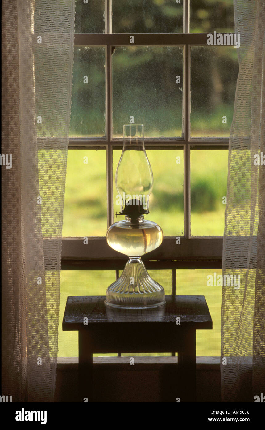 Una lámpara de aceite de vidrio transparente en la ventana de inicio con cortinas de encaje. Foto de stock