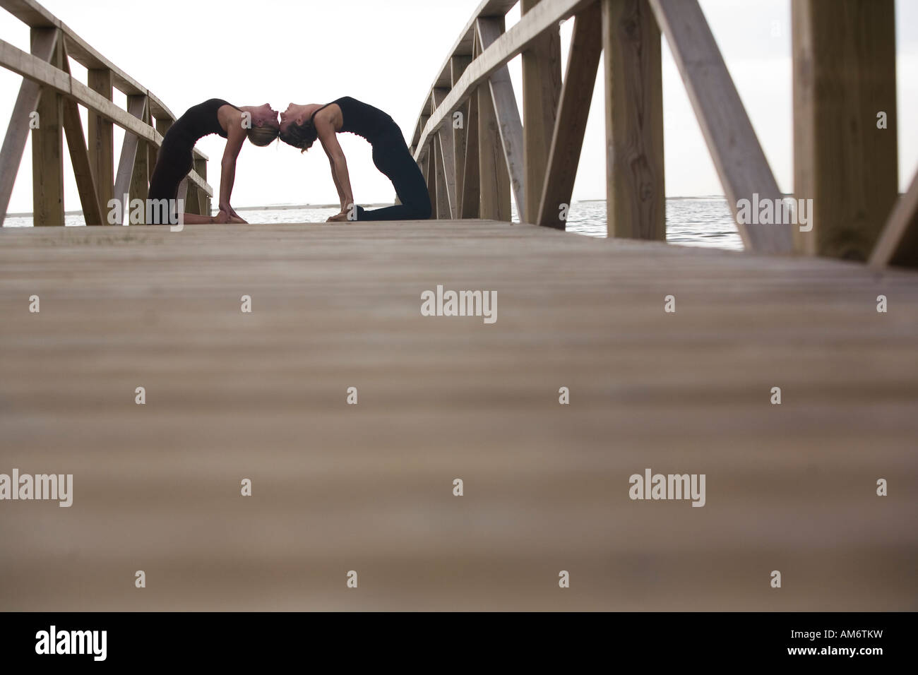 Dos mujeres practican yoga plantea sobre deck de madera en la naturaleza Foto de stock