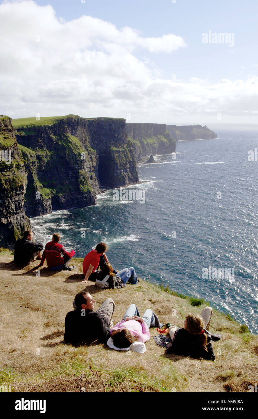 Jóvenes sentados en el borde de los Acantilados de Moher, en el condado de Clare oeste de Irlanda Foto de stock