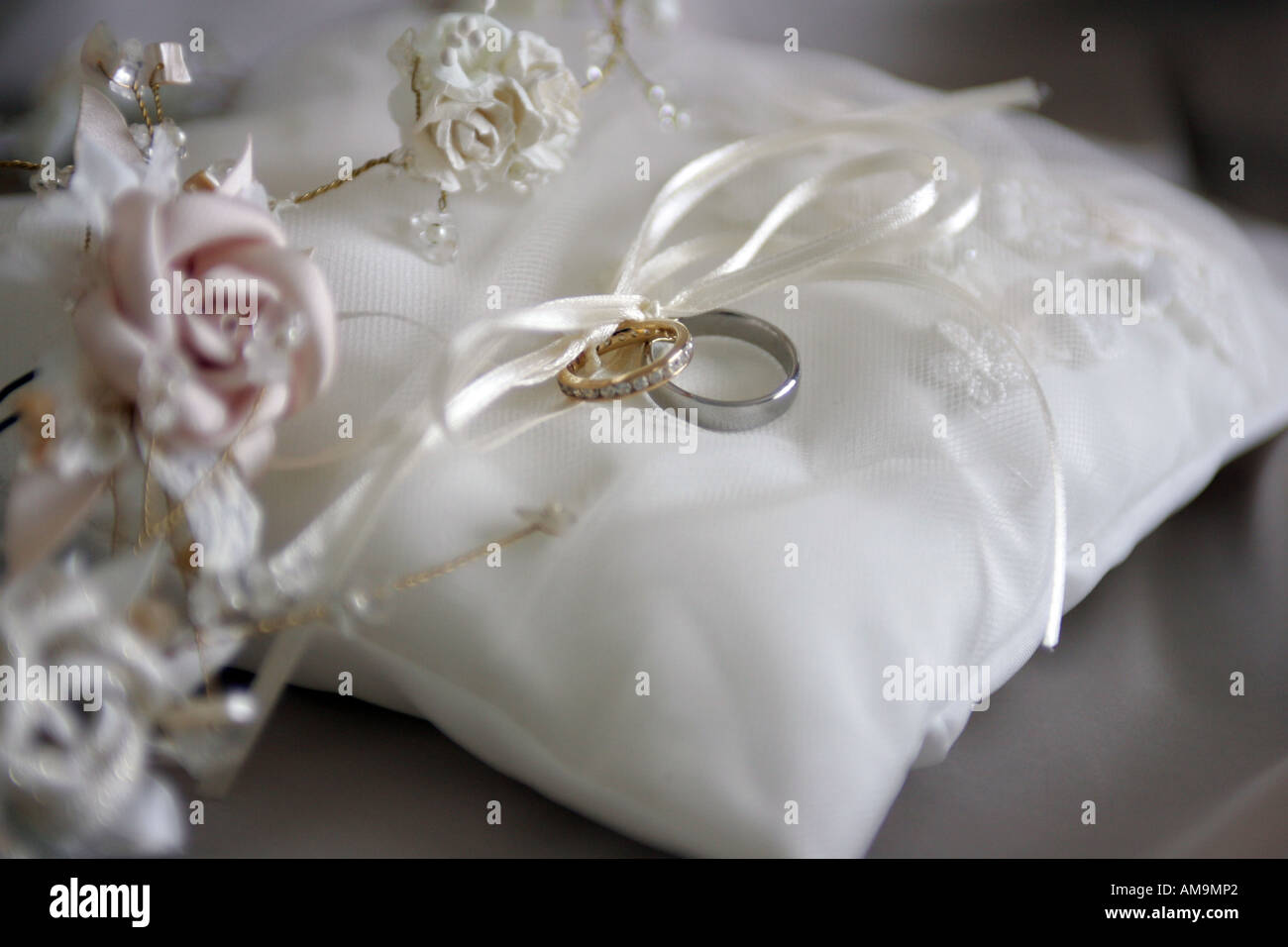 Un retrato de cerca de un anillo de bodas atado a una cinta blanca sobre un cojín blanco Foto de stock