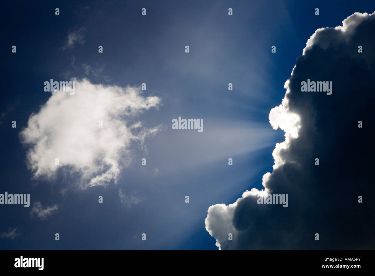 Haces de luz solar que brillan detrás de una nube contra el cielo azul Foto de stock