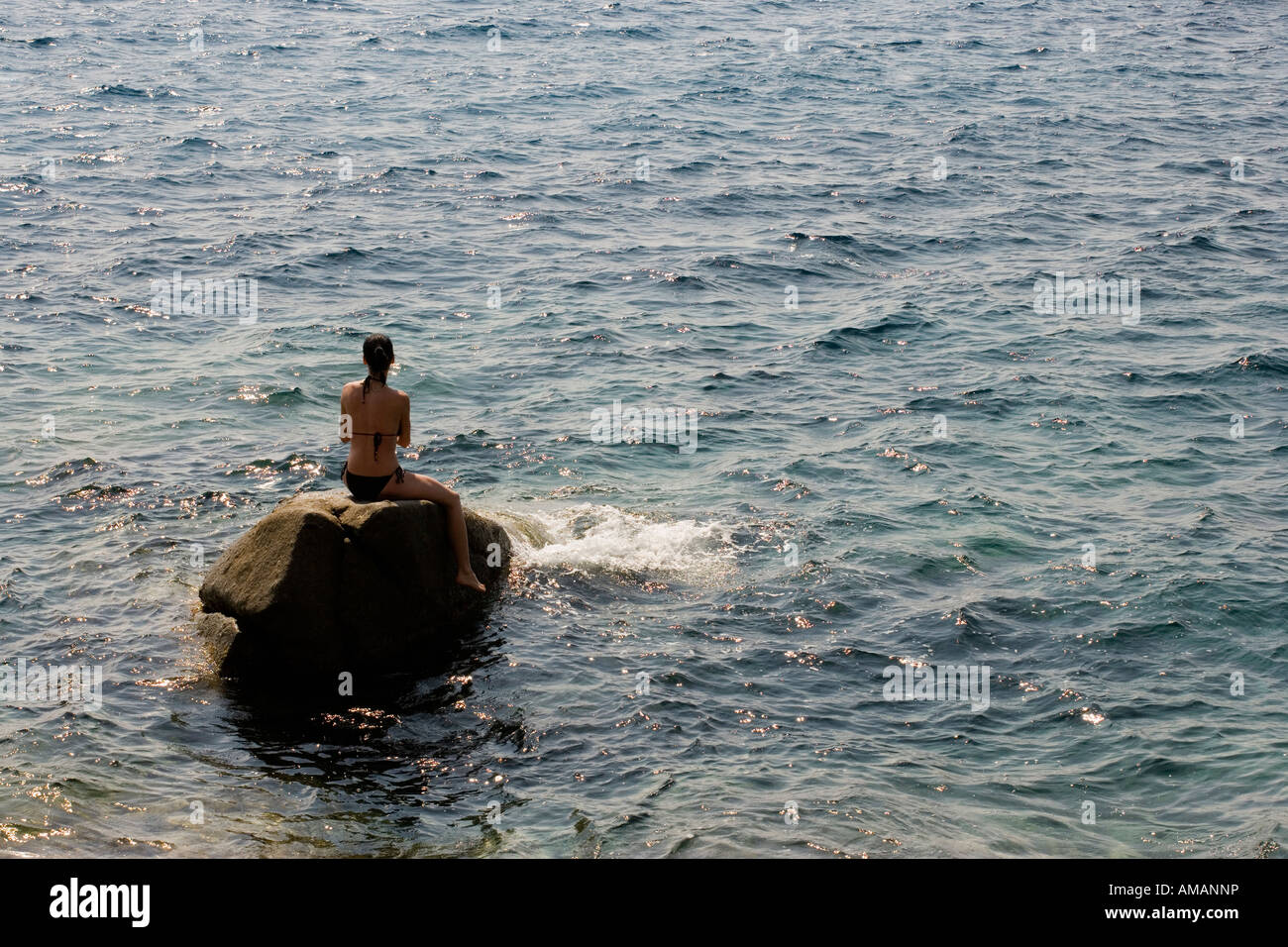 Una mujer sentada sobre una roca en el mar Foto de stock