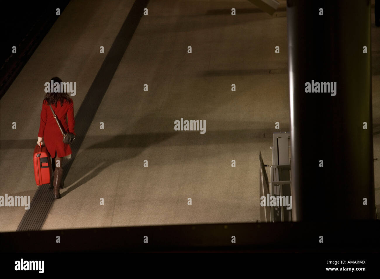 Una mujer que caminaba por una plataforma de estación en la noche con una maleta Foto de stock