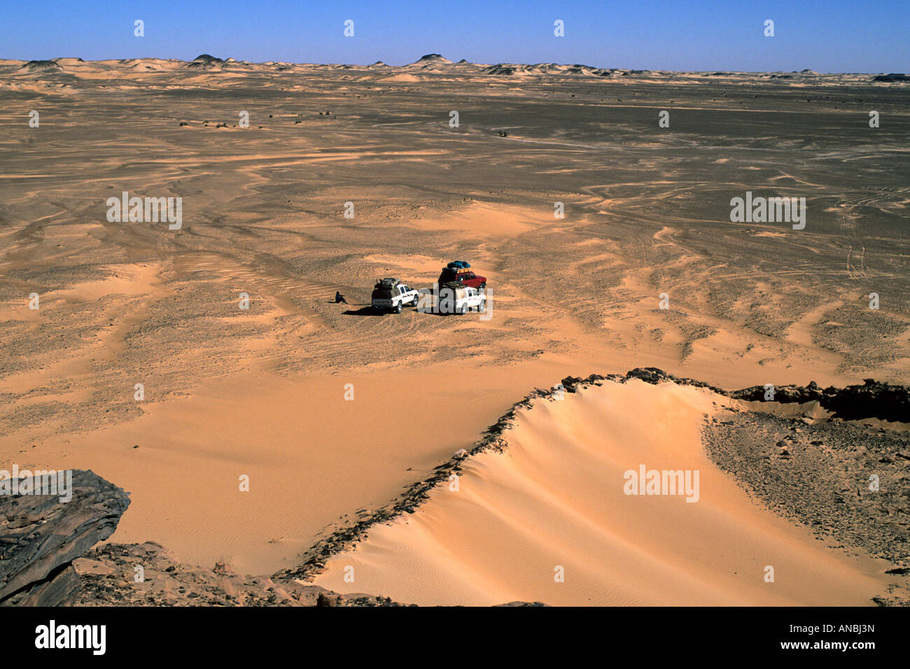 Tres vehículos cruzan la oscuridad desigual arenas del desierto cerca de Jebel Pick Foto de stock
