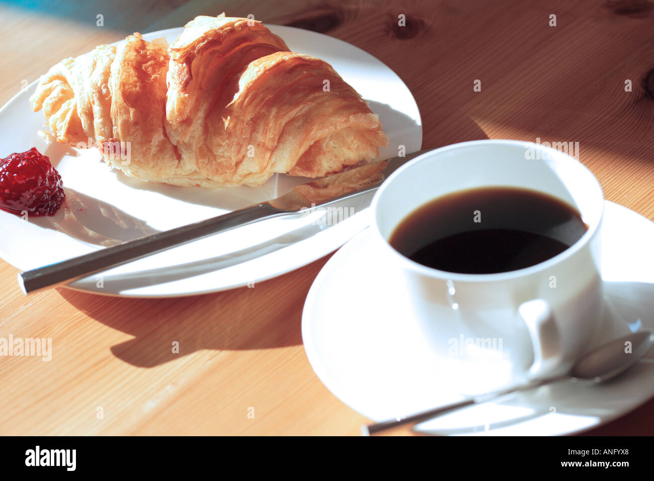 Café y un cruasán en vajilla de porcelana blanca en la luz del sol - horizontal Foto de stock