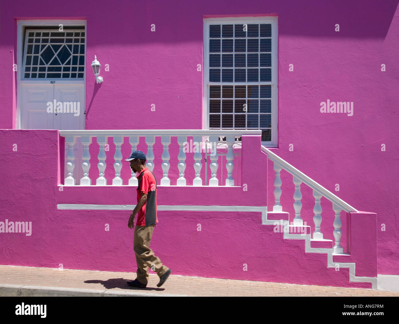 Hombre caminando pasado rosa brillante casa en el distrito de Bo Kaap de Cape Town South Africa Foto de stock