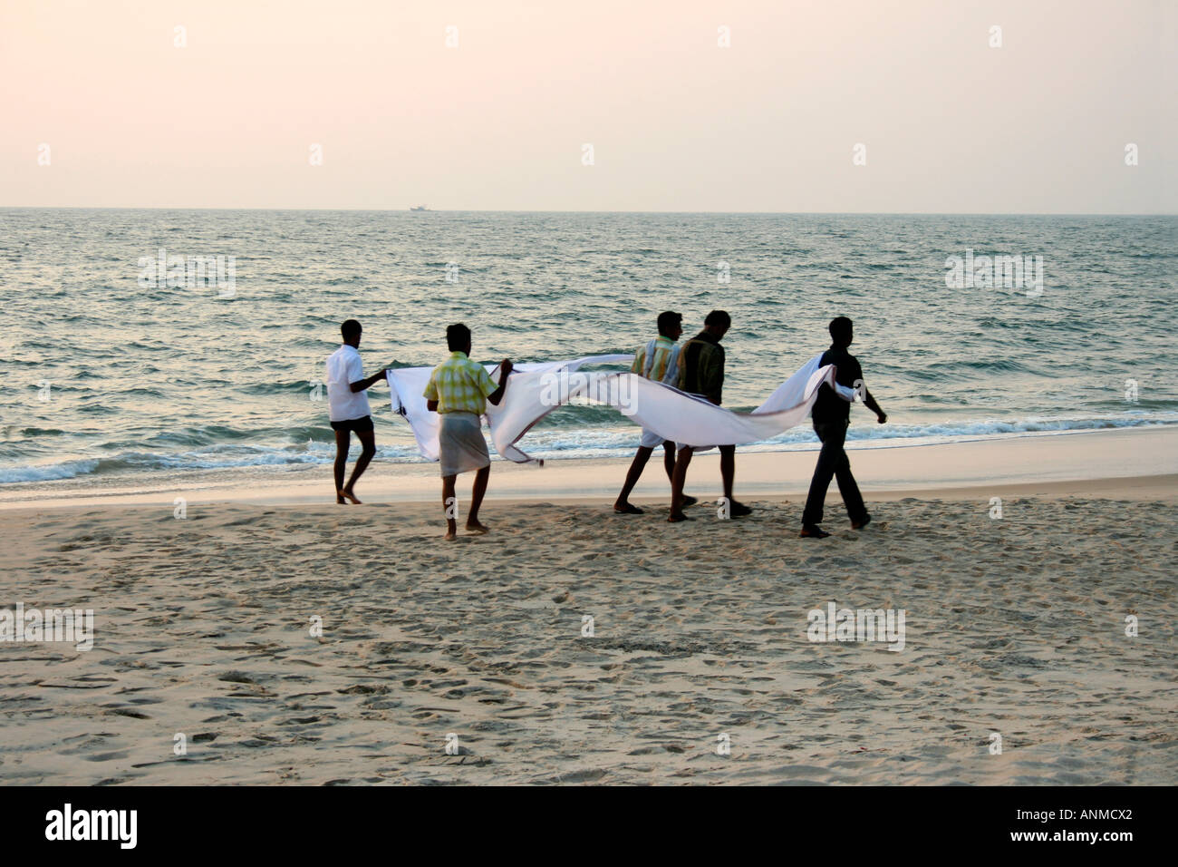 Hombres caminando por la playa llevando larga tela blanca para secar en Alappuzha Beach, Kerala Foto de stock