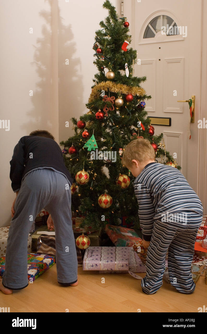 Dos niños abriendo regalos bajo el árbol en la mañana de Navidad en el  reino unido Fotografía de stock - Alamy
