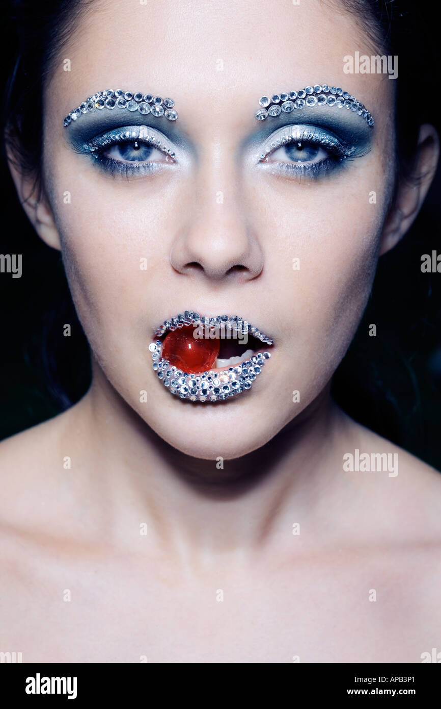 Frente a una hermosa chica con incrustaciones de diamantes de cejas y  labios, con una cereza en la boca Fotografía de stock - Alamy